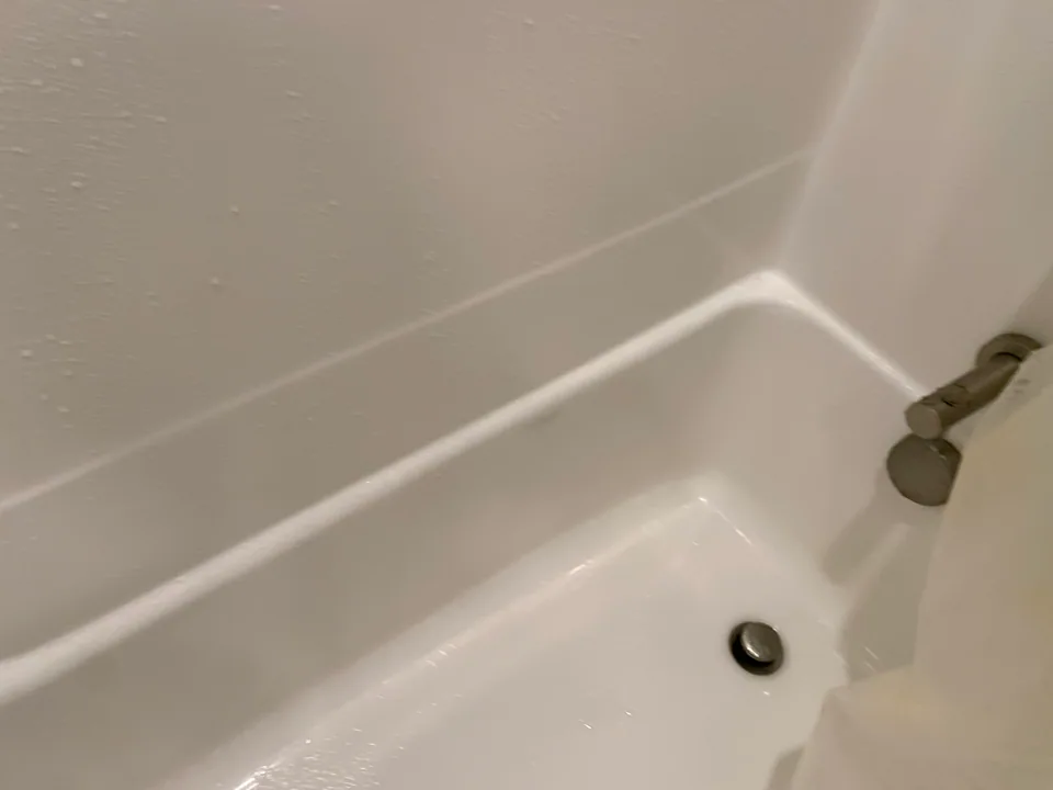 White bathtub basin and wall surround with a clear surface around the drain.